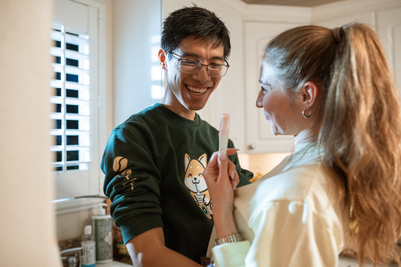 A joyful couple celebrating a positive pregnancy test result in a cozy kitchen.